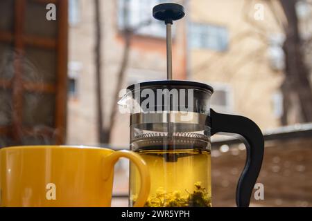 Teiera (pressa francese) con mezzo limone e teiera al tavolo di legno sul balcone, tè mattutino, aromaterapia aromatica fresca ed erboristica, tè biologico Foto Stock
