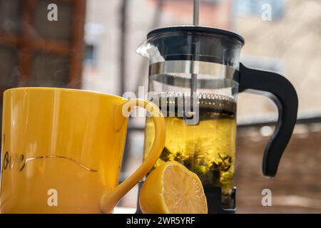 Teiera (pressa francese) con mezzo limone e teiera al tavolo di legno sul balcone, tè mattutino, aromaterapia aromatica fresca ed erboristica, tè biologico Foto Stock