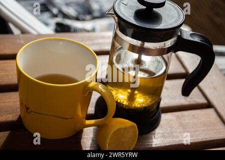 Teiera (pressa francese) con mezzo limone e teiera al tavolo di legno sul balcone, tè mattutino, aromaterapia aromatica fresca ed erboristica, tè biologico Foto Stock