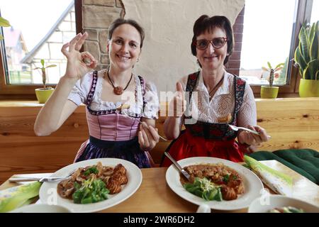 Tanne, Germania. 11 marzo 2024. Julia e sua madre Susanne Thielecke provano un pezzo di testicolo di toro arrosto nel ristorante Brockenbauer a Tanne. La nuova prelibatezza sarà presto aggiunta al menu del ristorante. Brockenbauer Thielecke a Tanne commercializza quasi il cento per cento del suo bestiame. Hanno creato una specialità insolita sotto forma di testicoli di toro, che devono essere serviti come ostriche di montagna. Crediti: Matthias Bein/dpa/Alamy Live News Foto Stock