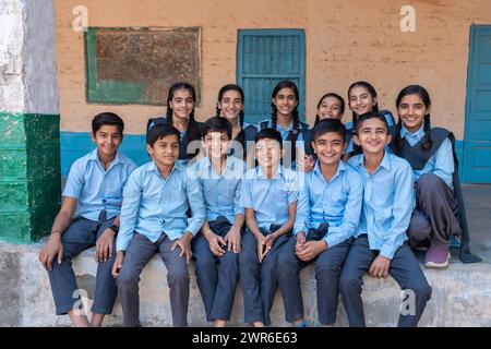 Gruppo di studenti delle scuole indiane rurali seduti insieme in uniforme blu che guardano la macchina fotografica Foto Stock