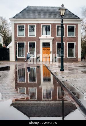 Un edificio residenziale su Dorpsstraat con una donna che cammina accanto a una grande pozzanghera riflettente a Zoetermeer Foto Stock