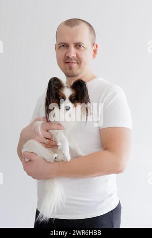 Uomo che tiene in mano il carino piccolo papillon cane sul bianco Foto Stock