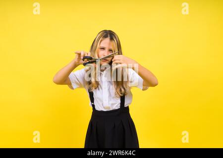 Ragazza scolastica adolescente con forbici, isolata su sfondo giallo. Creatività dei bambini, arti e mestieri. Foto Stock