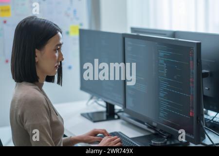 I tecnici asiatici sviluppano un'applicazione di codifica con dati software posizionati davanti al monitor del computer in ufficio Foto Stock