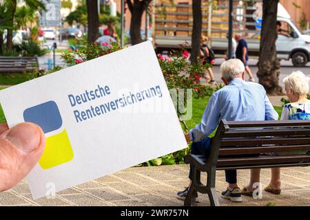 Germania - 11 marzo 2024: Logo tedesco dell'assicurazione pensionistica su un cartello tenuto da una mano davanti ad una coppia di pensionati. FOTOMONTAGGIO *** Deutsche Rentenversicherung Logo auf einem Schild das von einer Hand gehalten wird vor einem alten Rentner Ehepaar. FOTOMONTAGE Foto Stock