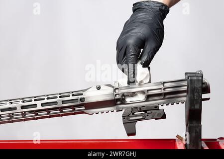 Mano dell'uomo nel guanto pulizia con tovagliolo la pistola di metallo in piedi su un supporto di plastica rosso sfondo grigio Foto Stock