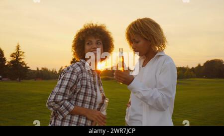 Felice multirazziale giovani ragazze africane multietniche con capelli afro che si divertono e bevono alcune birre all'aperto in estate al tramonto dorato Foto Stock