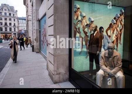 Immagini pubblicitarie con diverse donne in costume da bagno in formazione per il rivenditore di moda Suit Supply che interagiscono con manichini maschili nella vetrina del negozio mentre le persone passano a Mayfair il 6 marzo 2024 a Londra, Regno Unito. Foto Stock