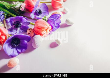 Buona Pasqua. Le uova di Pasqua con fiori viola rosa primaverile sono piatte su sfondo viola. Biglietto d'auguri o striscione con fiori. Spazio. Vista dall'alto Foto Stock