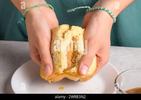 le mani della donna rompono un panino con miele e burro di arachidi di pane di grano su un piatto bianco, per fare colazione, da vicino. Snack tipici, cibo Foto Stock