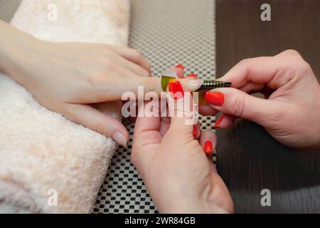 Il maestro dello smalto per unghie mette un fissativo sul dito prima di preparare il gel per unghie nel salone di bellezza. Cura professionale delle mani. Foto Stock