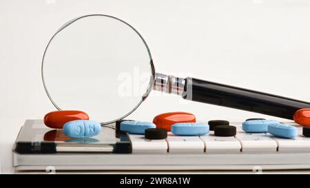 Una lente d'ingrandimento su una calcolatrice con tavolette su sfondo bianco. Una foto concettuale. Un luogo da copiare. Foto Stock