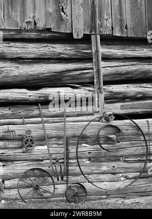 Vecchi macchinari rustici rustici agricoli di fronte alla capanna di tronchi muro esterno del capannone in una fattoria rurale nella campagna cinta di tronchi in bianco e nero Foto Stock