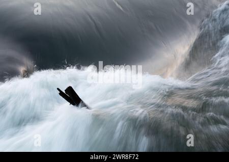 Bastoncino di legno in acqua turbolenta, flusso d'acqua rapido e ondulato da vicino, paesaggio astratto con sfocatura in movimento Foto Stock