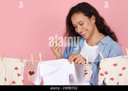 donna positiva giovane madre che mette i vestiti per bambini su un asciugatore Foto Stock