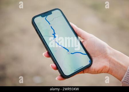 Primo piano di una mano che tiene in mano uno smartphone che visualizza una mappa di navigazione GPS, che indica un percorso per il viaggio o l'avventura in un ambiente all'aperto Foto Stock