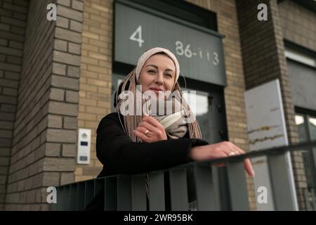 Donna simpatica e sorridente con dreadlock biondi che indossa una lunga giacca invernale nera Foto Stock