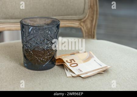 Un vetro blu tagliato con liquido ambrato all'interno accanto a un tampone di banconote in euro Foto Stock