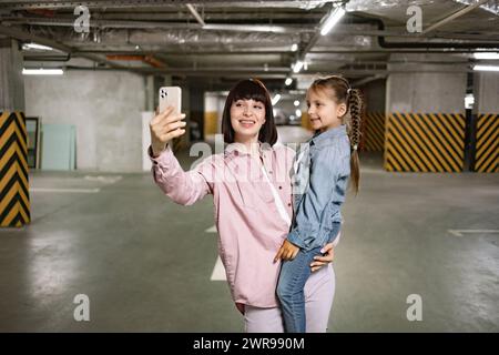 Madre caucasica che tiene in mano la figlia in età prescolare facendo selfie. Foto Stock