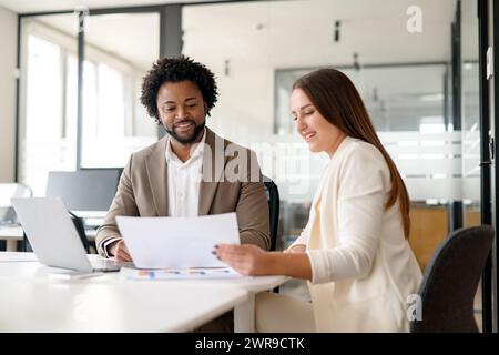 Due colleghi di lavoro impegnati in una discussione costruttiva con particolare attenzione alla documentazione cartacea, il che significa lavoro di squadra e cooperazione in un ambiente aziendale. Foto Stock