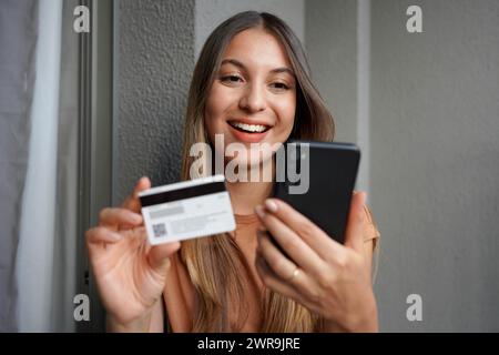 Primo piano di un'attraente ragazza ispanica fa acquisti su smartphone con carta di credito Foto Stock