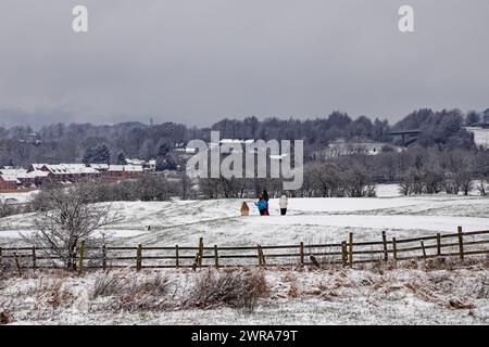 Una famiglia cammina attraverso un campo da golf innevato con case e boschi sullo sfondo a Walmersley, Bury, Greater Manchester. Foto Stock