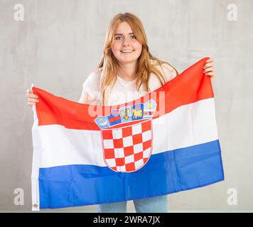 Una ragazza sorridente in braccio sollevata sopra la testa tiene un panno di bandiera nazionale della Croazia Foto Stock