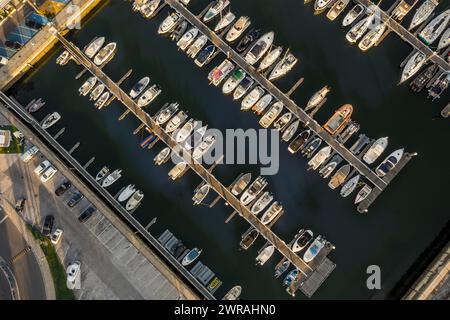 Vista aerea dall'alto verso il basso di una fila di yacht, barche a vela e jet nel porticciolo con barche a vela ormeggiate. Sole basso, sole, drone rimangono e salgono rivelando più vasi. Foto Stock