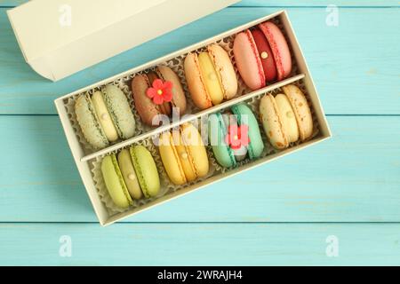 Macaron multicolore in una scatola di cartone bianca su uno sfondo di legno blu chiaro. Primo piano. Vista dall'alto verso il basso. Foto Stock