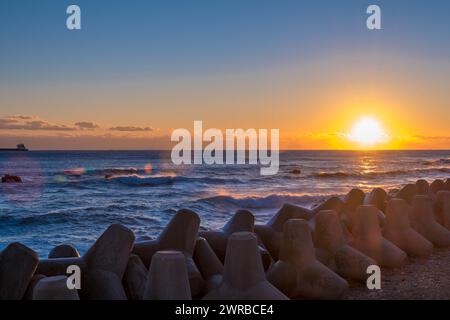 Cielo ambrato all'alba sul mare con tetrapodi e onde morbide che colpiscono la riva, in Corea del Sud Foto Stock