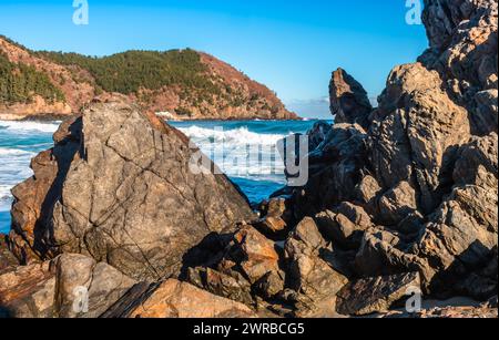 Onde schiumose che colpiscono le coste rocciose di un mare blu vibrante in una giornata di sole con un cielo limpido, in Corea del Sud Foto Stock
