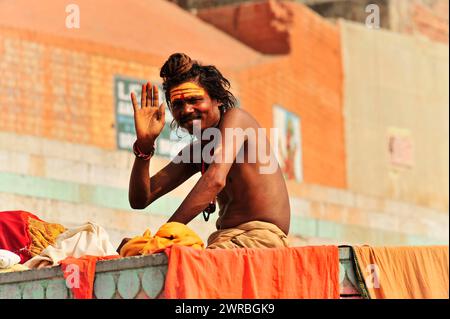 Un sadhu ai ghati di Varanasi saluta con un volto dipinto e abiti tradizionali, Varanasi, Uttar Pradesh, India Foto Stock