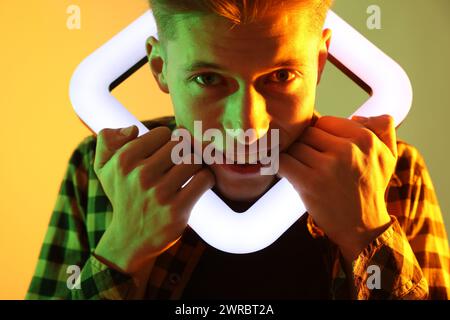 Giovane uomo con lampada quadrata su sfondo colorato con luci al neon Foto Stock