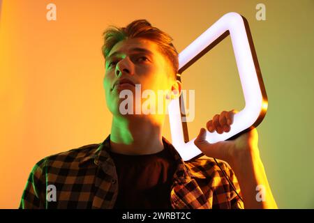 Giovane uomo con lampada quadrata su sfondo colorato con luci al neon Foto Stock