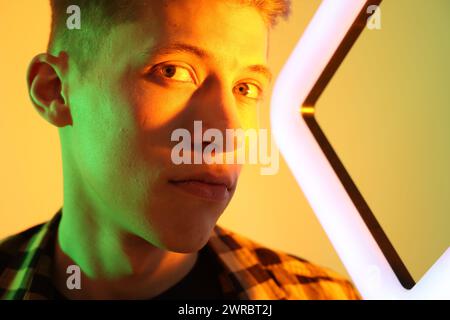 Giovane uomo con lampada quadrata su sfondo colorato con luci al neon Foto Stock