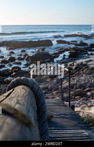 Una verticale di una passerella di legno che conduce giù ad una spiaggia rocciosa Foto Stock