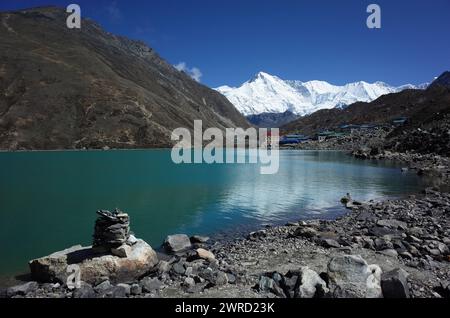 Piramide di pietra accanto al sacro lago Gokyo con vista del villaggio di Gokyo e del monte Cho Oyu. Escursioni in Nepal, Himalaya Foto Stock