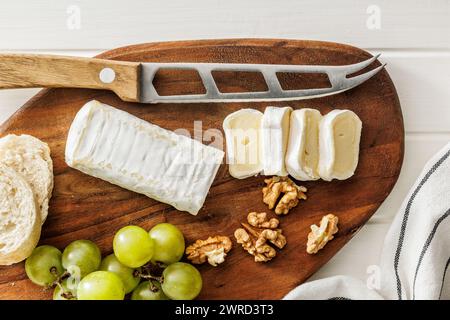 Formaggio Brie artigianale tagliato su un tagliere rotondo in legno, servito con uva e noci, immagine ideale per i concetti di formaggio Gourmet Foto Stock