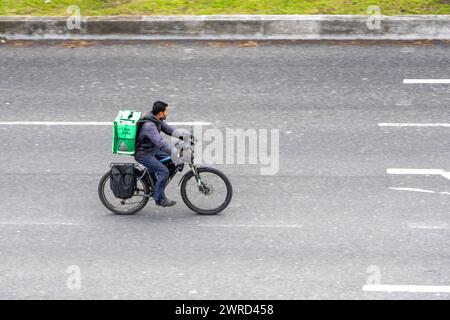 Lisbona, Portogallo l'11 marzo 2024, il dipendente di Uber Eats viaggia su strada a Lisbona con una bicicletta elettrica senza protezione o segnalazione luminosa Foto Stock