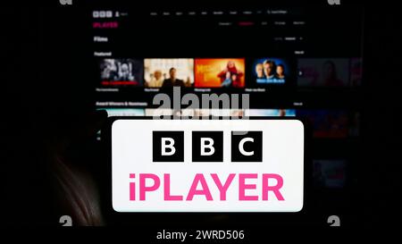 Persona che detiene un cellulare con il logo del servizio di video on demand britannico BBC iPlayer davanti alla pagina web aziendale. Mettere a fuoco il display del telefono. Foto Stock