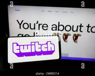 Persona che possiede uno smartphone con il logo della società di live streaming statunitense Twitch Interactive Inc. Davanti al sito Web. Mettere a fuoco il display del telefono. Foto Stock