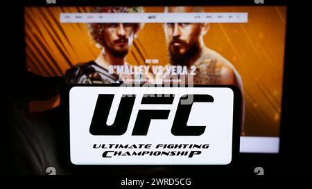 Persona che detiene un cellulare con il logo della società di arti marziali Ultimate Fighting Championship (UFC) davanti alla pagina web. Mettere a fuoco il display del telefono. Foto Stock