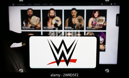 Persona che possiede un cellulare con il logo della società di promozione World Wrestling Entertainment (WWE) di fronte alla pagina Web aziendale. Mettere a fuoco il display del telefono. Foto Stock