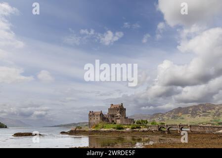 Il castello di Eilean Donan emerge dalle acque del lago scozzese, il suo storico ponte adagiato sull'arazzo delle Highlands e con un cielo dipinto Foto Stock