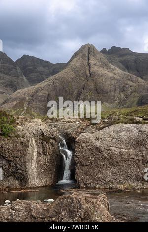 Una cascata si estende attraverso le rocce aspre presso le Fairy Pools, l'Isola di Skye, adagiata contro le imponenti montagne Cuillin (tiro verticale) Foto Stock