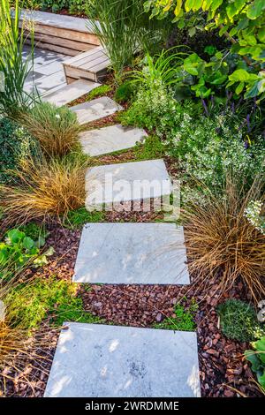 Sentiero del giardino con lastre di pietra con pacciame di corteccia e piante autoctone. Concetto di architettura paesaggistica e giardinaggio. Foto Stock