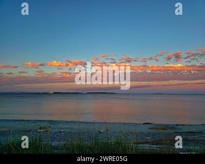 Il tramonto diffonde una luce calda sull'erba costiera e sull'acqua Foto Stock