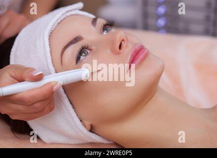 Il medico-cosmetologo effettua la procedura di trattamento di Couperose della pelle del viso di una bella, giovane donna in un salone di bellezza Foto Stock