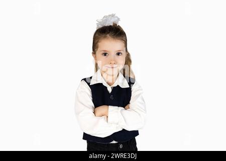 Una bambina con l'uniforme scolastica, completa di camicia, blazer e cravatta, sta in piedi con le braccia incrociate e indossa un sorriso sul viso Foto Stock